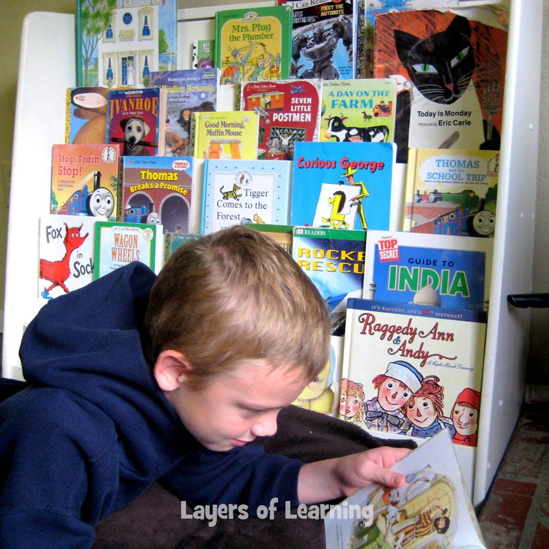 Young boy reading with bookshelf full of picture books behind him